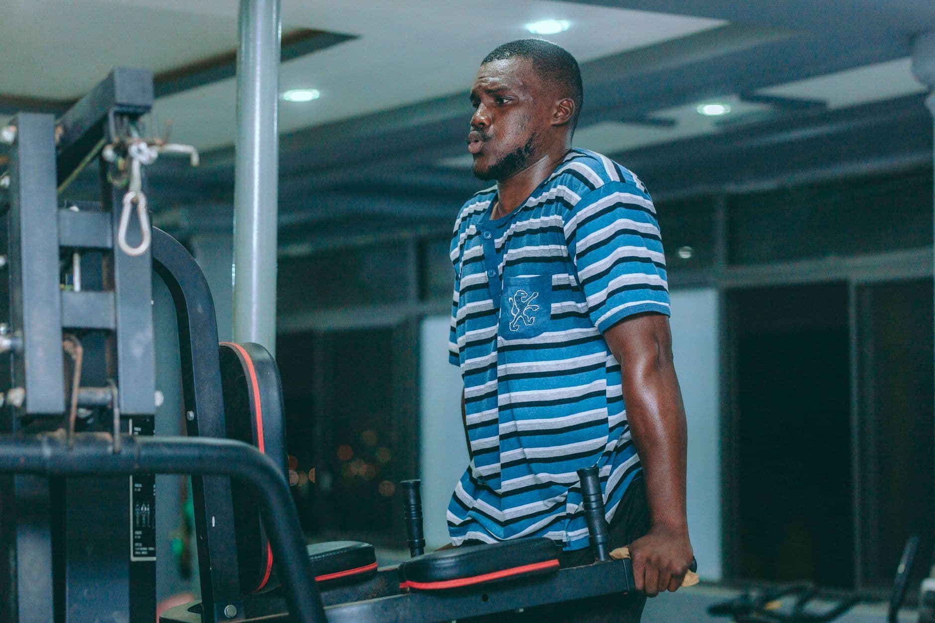 A man wearing stripes focuses on strength training at a gym in Accra, Ghana.