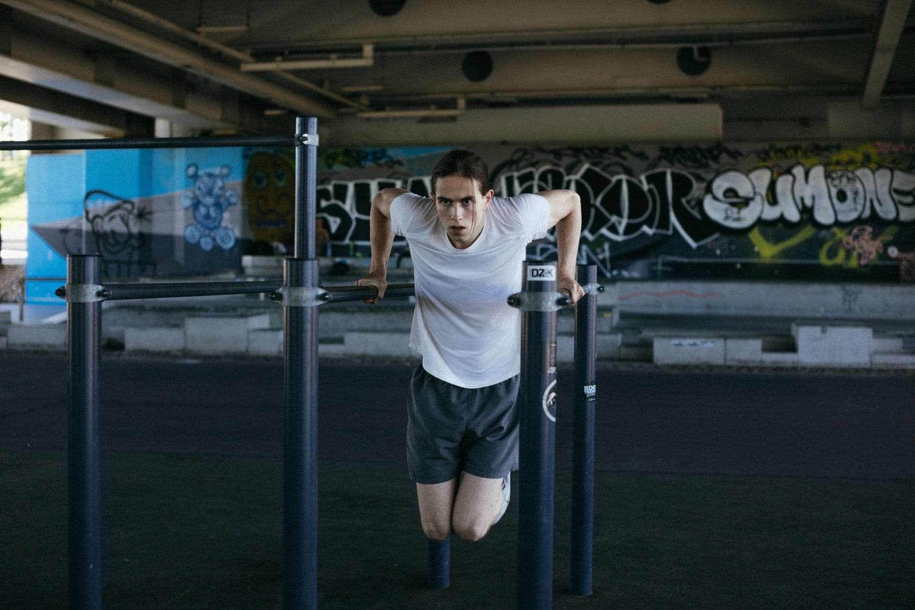 Athletic man in urban setting exercises on bars with vibrant graffiti background, showcasing flexibility.